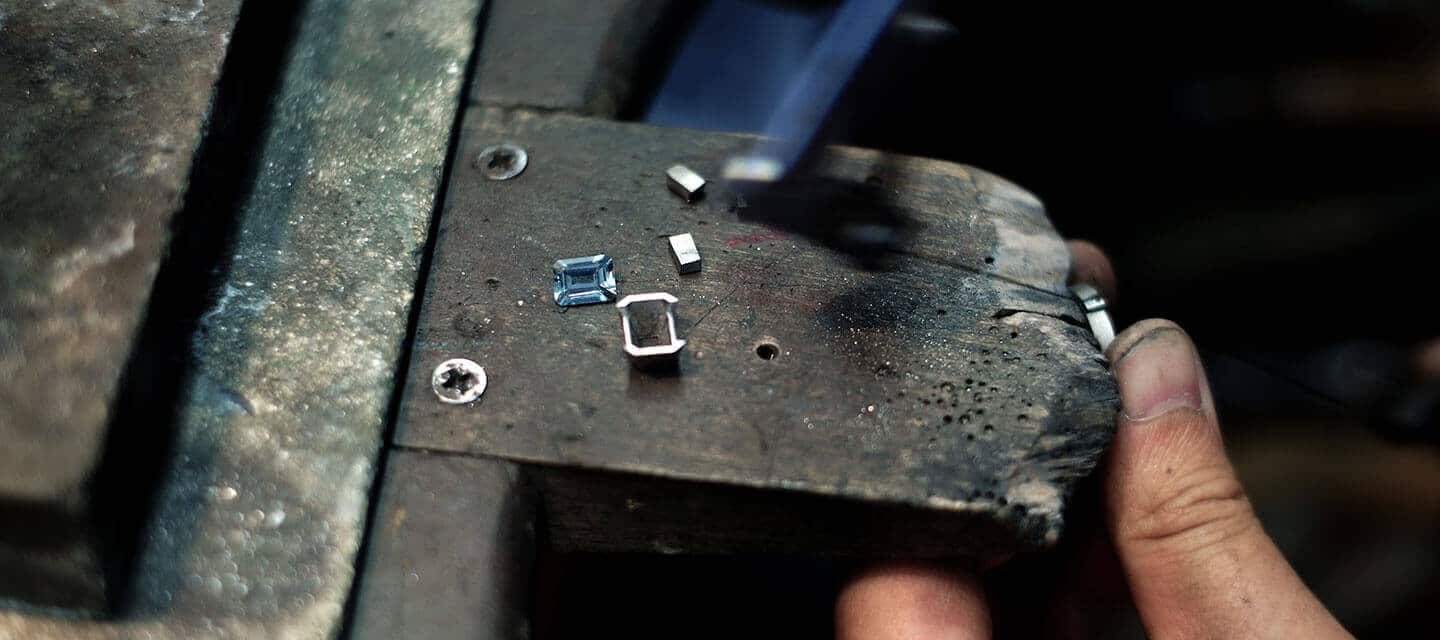 closeup of goldsmith sawing aquamarine engagement ring