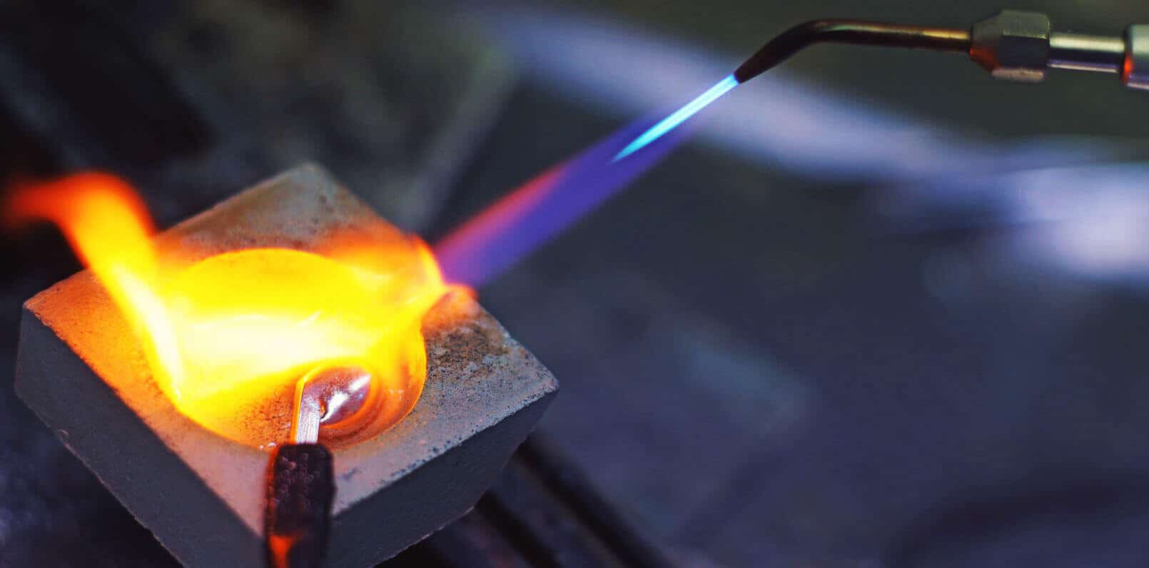 Blowtorch flame melting metal in a crucible