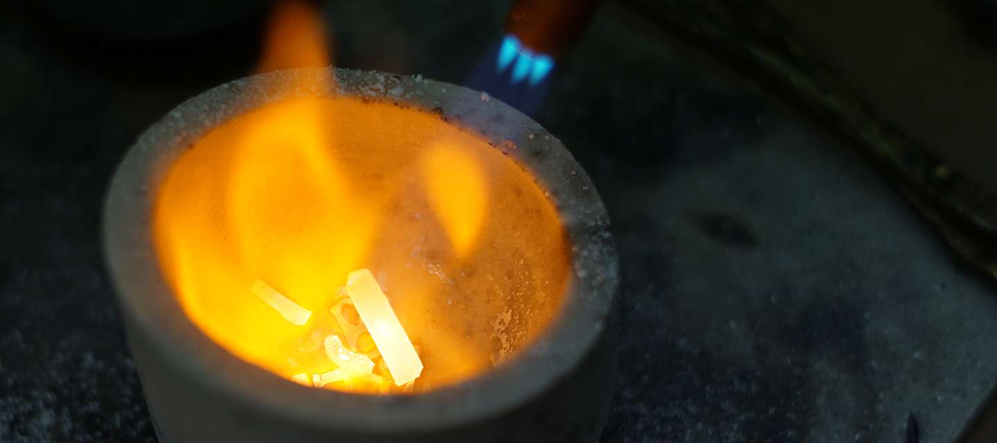 Blowtorch flame melting metal in a crucible