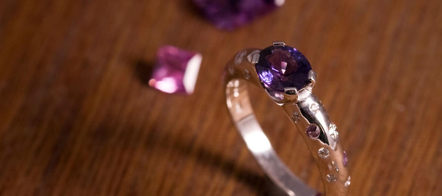 Purple amethyst ring with pink gemstone in the background