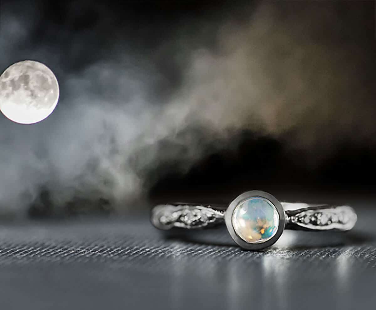 Moonstone ring with a crescent moon and dark clouds in the background, showcasing a mystical and ethereal design.