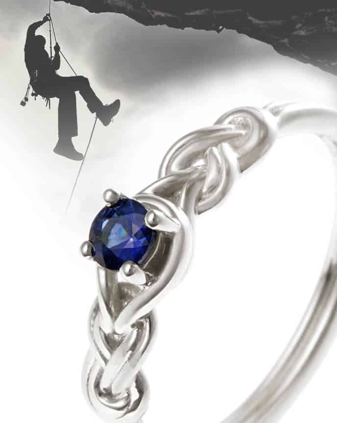 Rope climbing knotted rope shaped engagement ring with rock climber in the background - sapphire gemstone