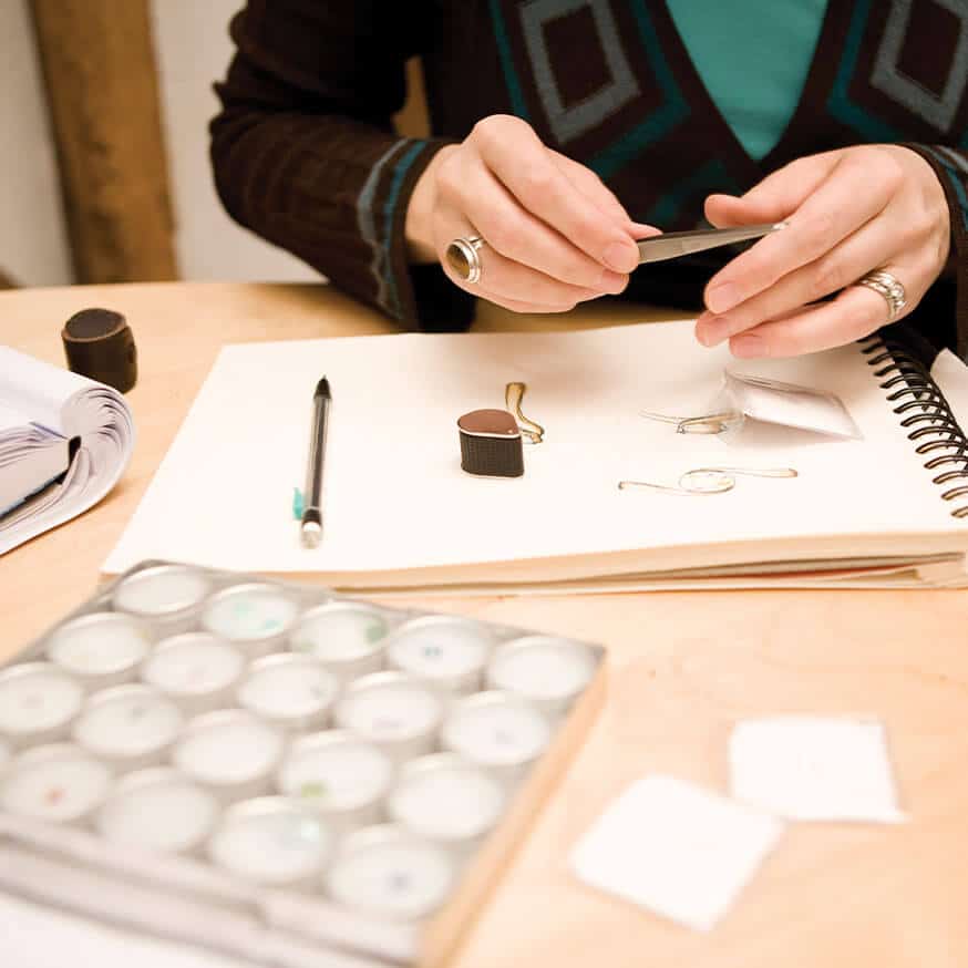 diamond in tweezers on desk with gemmologist equipment