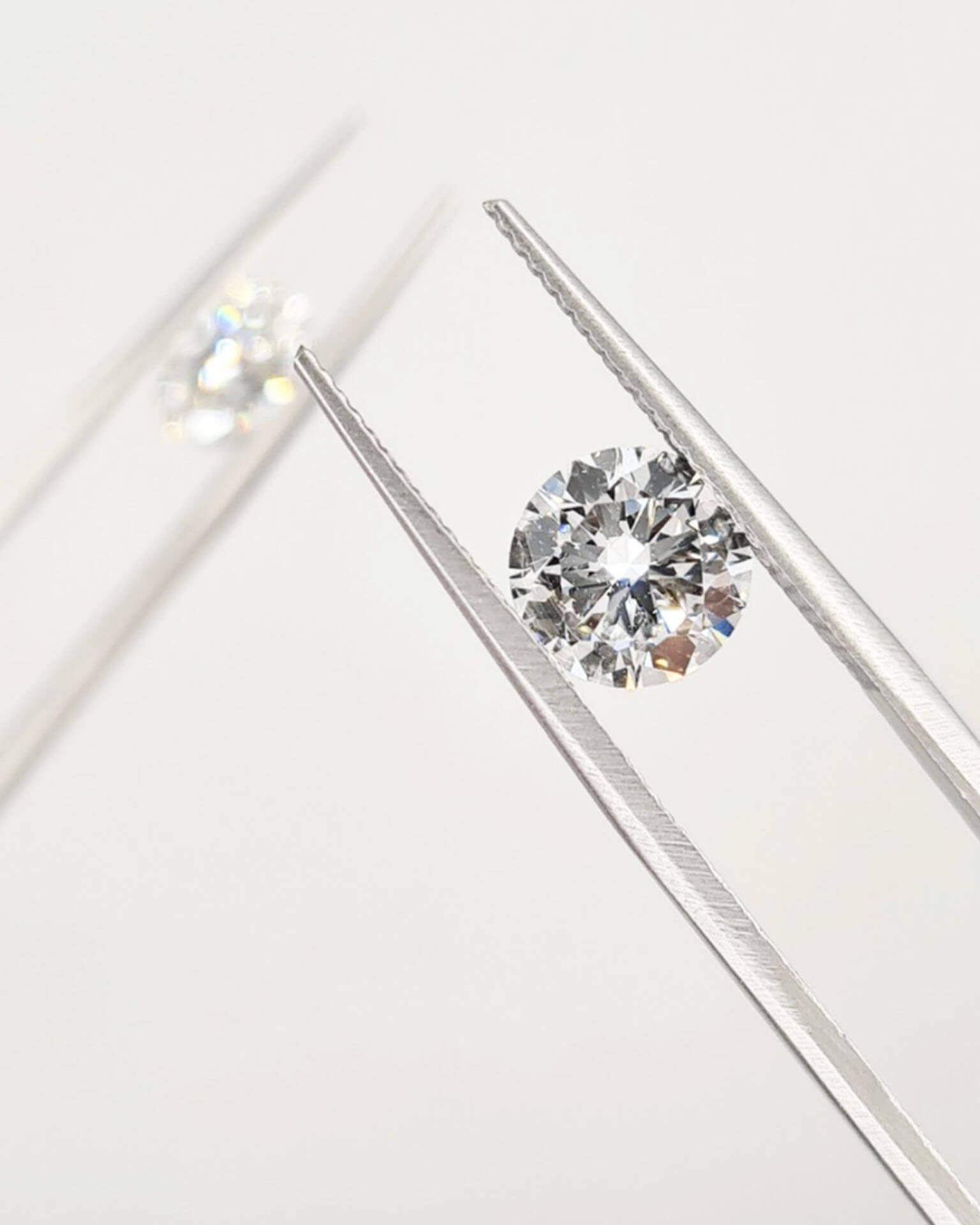 Diamonds in tweezers with a second blurred out diamond in tweezers behind