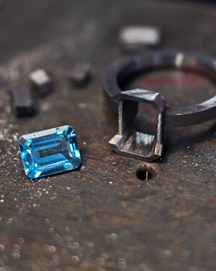 loose blue gemstone and unfinished ring on bench