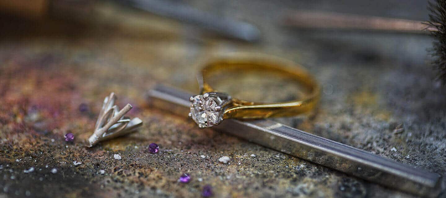 Gold diamond solitaire on workbench with a claw holding a gem and a meta claw lying in front of it and tiny purple gems