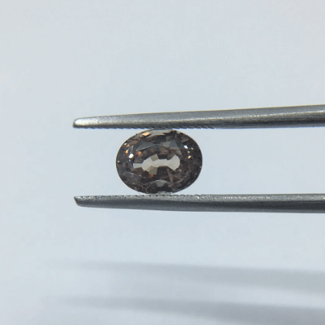 Grey oval spinel in tweezers