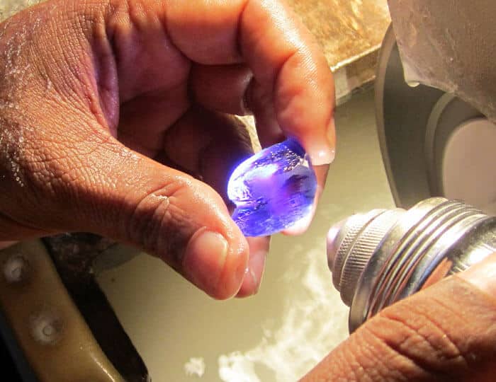 blue gemstone being cut by hand with water