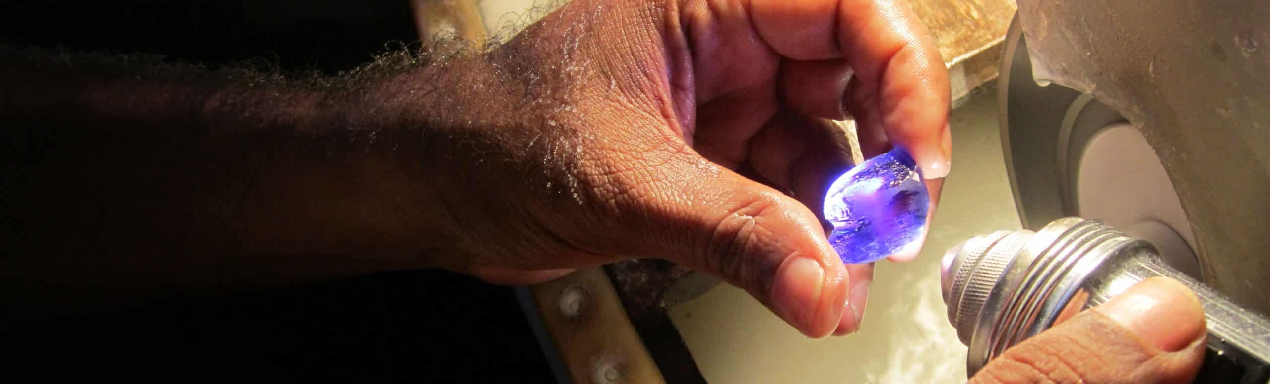 blue gemstone being cut by hand with water